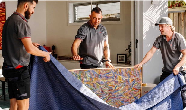 Team members moving a wrapped rug indoors